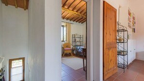 A hallway with a wooden door, a metal shelf unit, and a wicker chair. - Cosy apartment for 4 people with WIFI, TV, patio, pets allowed and panoramic view (Gavorrano)