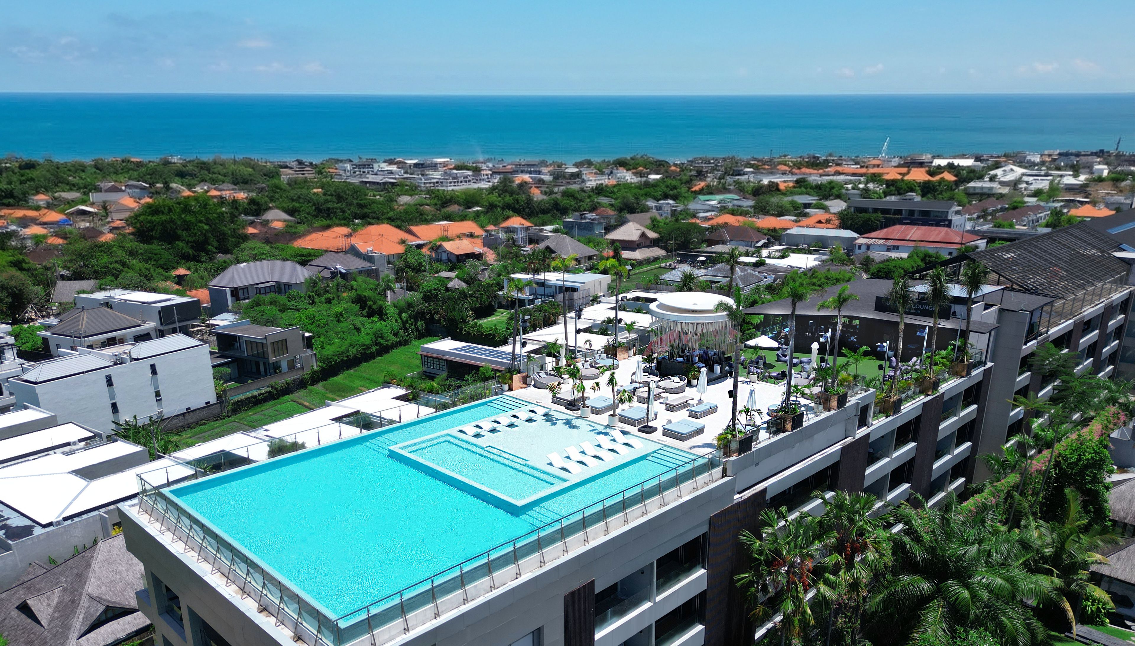 A hotel with a rooftop pool, multiple floors, and a view of the ocean.