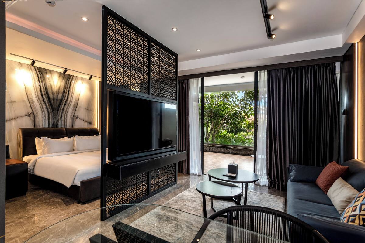Una habitación de hotel moderna con una cama grande, un televisor de pantalla plana, un sofá, una mesita y un balcón con cortinas.
