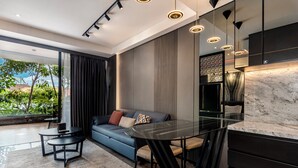 Ein modernes Wohnzimmer mit einem Glastisch, einem blauen Sofa und Blick auf Grünfläche.