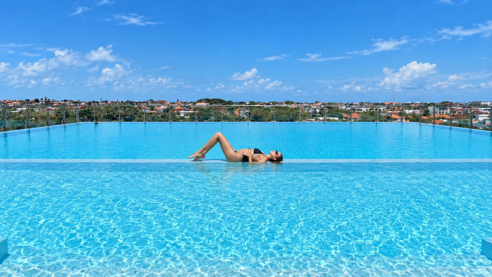 A person lying on a clear blue pool with a view of a residential area in the background.