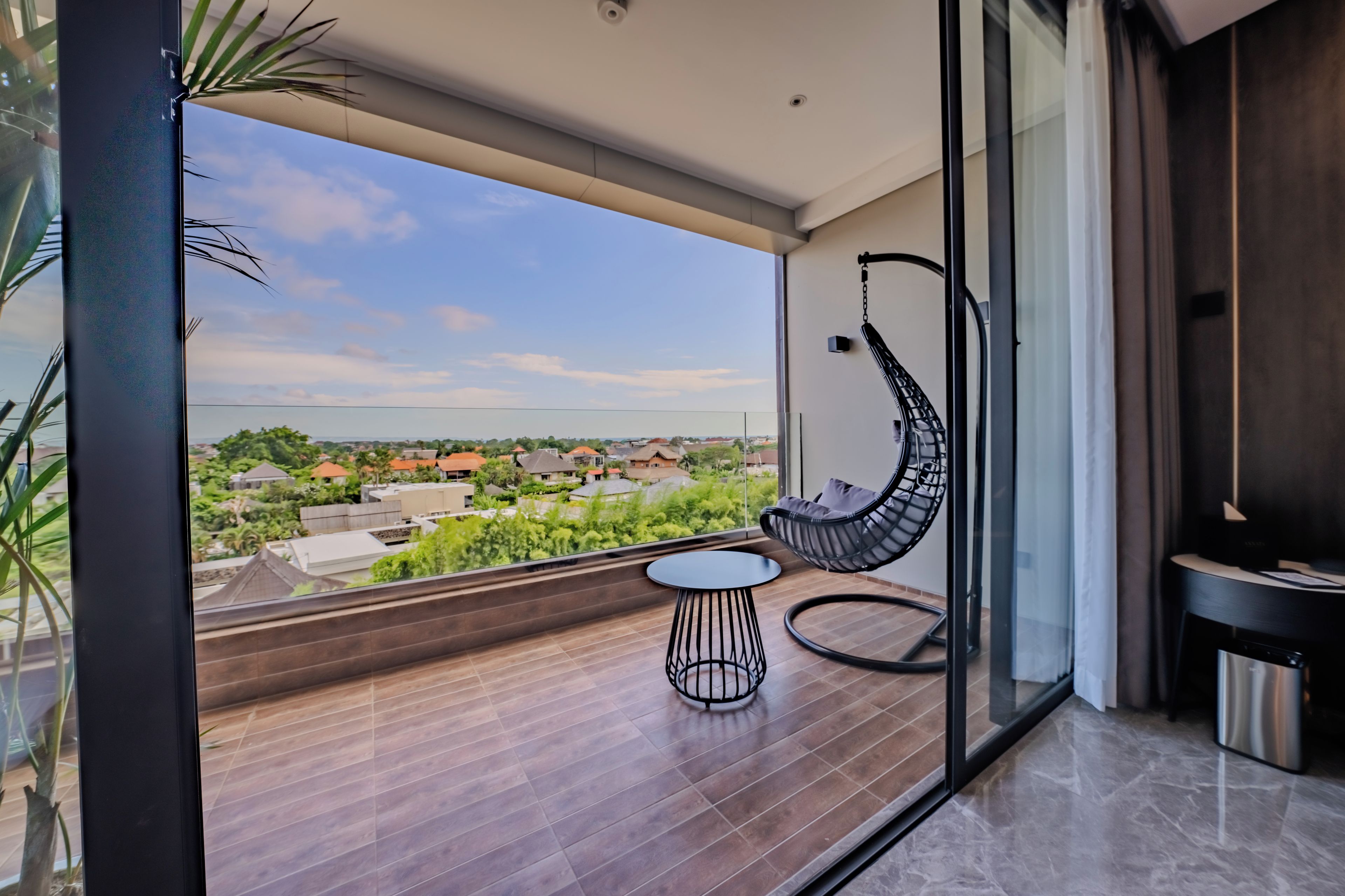 A balcony with a hanging chair, a small round table, and a view of a residential area.