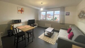 A compact living space with a dining table, a sofa, a TV, and a window with a city view. - L'Héloïse, studio à Arras en résidence sécurisée (Arras)
