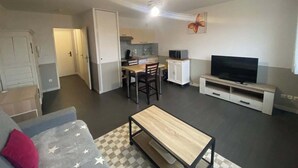 A compact living space with a kitchenette, a dining area, a TV, and a sofa. - L'Héloïse, studio à Arras en résidence sécurisée (Arras)