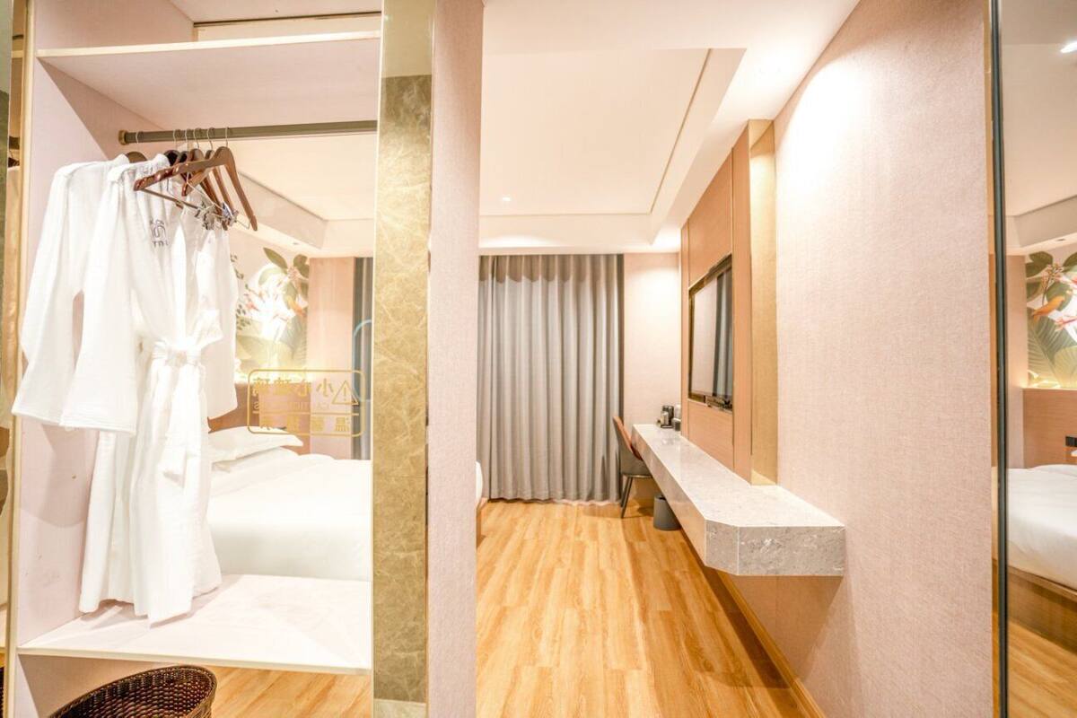 A modern hotel room with a wooden floor, a large mirror, a vanity with a marble countertop, and a hanging robe rack.