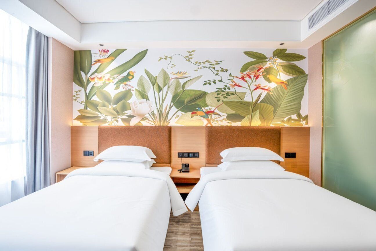Habitación de hotel con dos camas, un mural floral en la pared y vistas a la ciudad.
