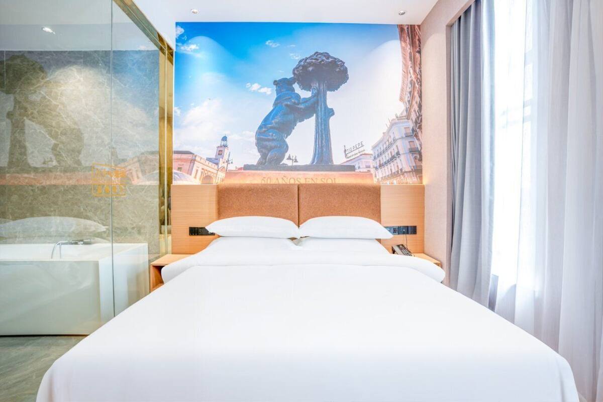 A hotel room with a large bed, a glass shower enclosure, and a mural of a statue on the wall.