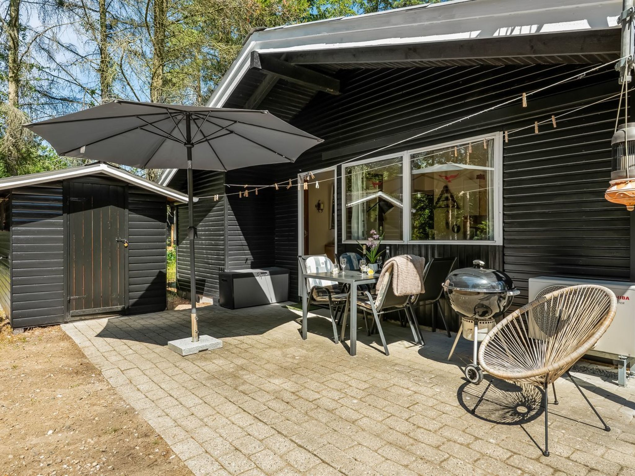 Eine Terrasse mit Grill, Gartenmöbeln und einem überdachten Bereich mit Sonnenschirm.