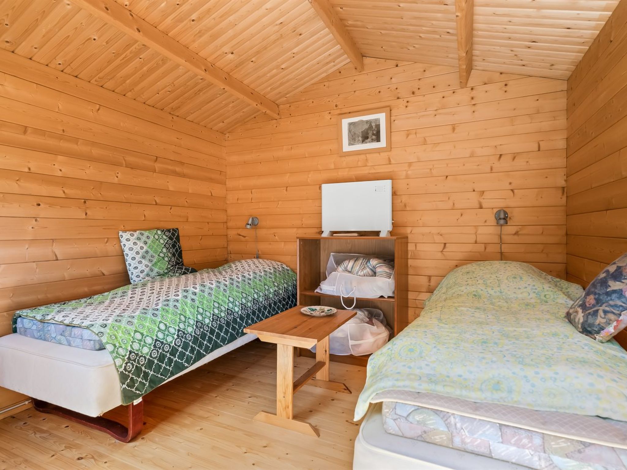 A cabin with two beds, a small table, a heater, and a framed picture on the wall.