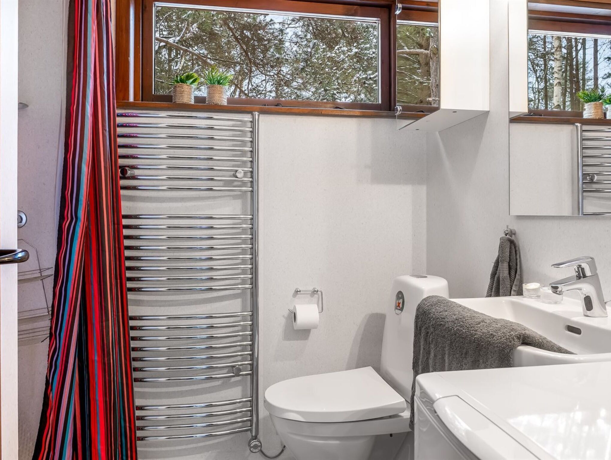 Een badkamer met douche, toilet, wastafel en een raam met planten.