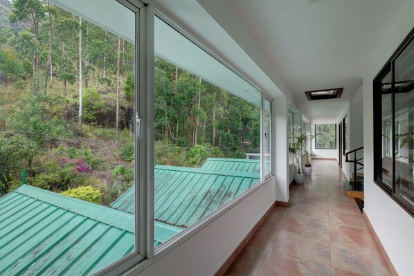 Un pasillo con amplias ventanas, suelo de baldosas y vistas a una zona boscosa.