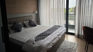 A modern bedroom with a large bed, a headboard, a bedside table, and a chair. - The Vilton (Raipur)