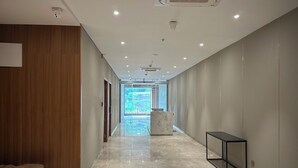 A modern hotel corridor with a marble floor, wooden panel walls, and a glass partition leading to a courtyard. - The Vilton (Raipur)