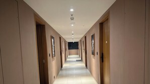 A long, narrow hallway with doors on both sides, recessed lighting, and a tiled floor. - The Vilton (Raipur)