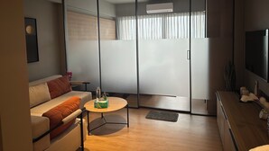 A modern living room with a sofa, a coffee table, a sliding glass door, a flat-screen TV, and a small plant on the coffee table. - The Vilton (Raipur)