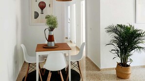Un espace repas comprenant une table, des chaises, un luminaire suspendu, un tableau encadré et une plante en pot.