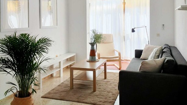 Un salon moderne comprenant un canapé, une table basse, un fauteuil et une grande fenêtre ornée de rideaux légers.
