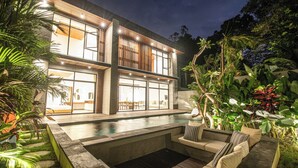 Ein modernes, zweistöckiges Haus mit Swimmingpool und Außenbereich zum Sitzen.