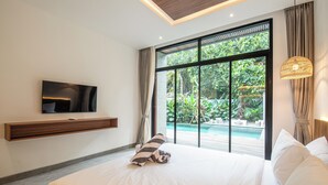 Ein Schlafzimmer mit einem großen Bett, einem an der Wand montierten Fernseher, Blick auf einen Swimmingpool und einer Hängelampe.