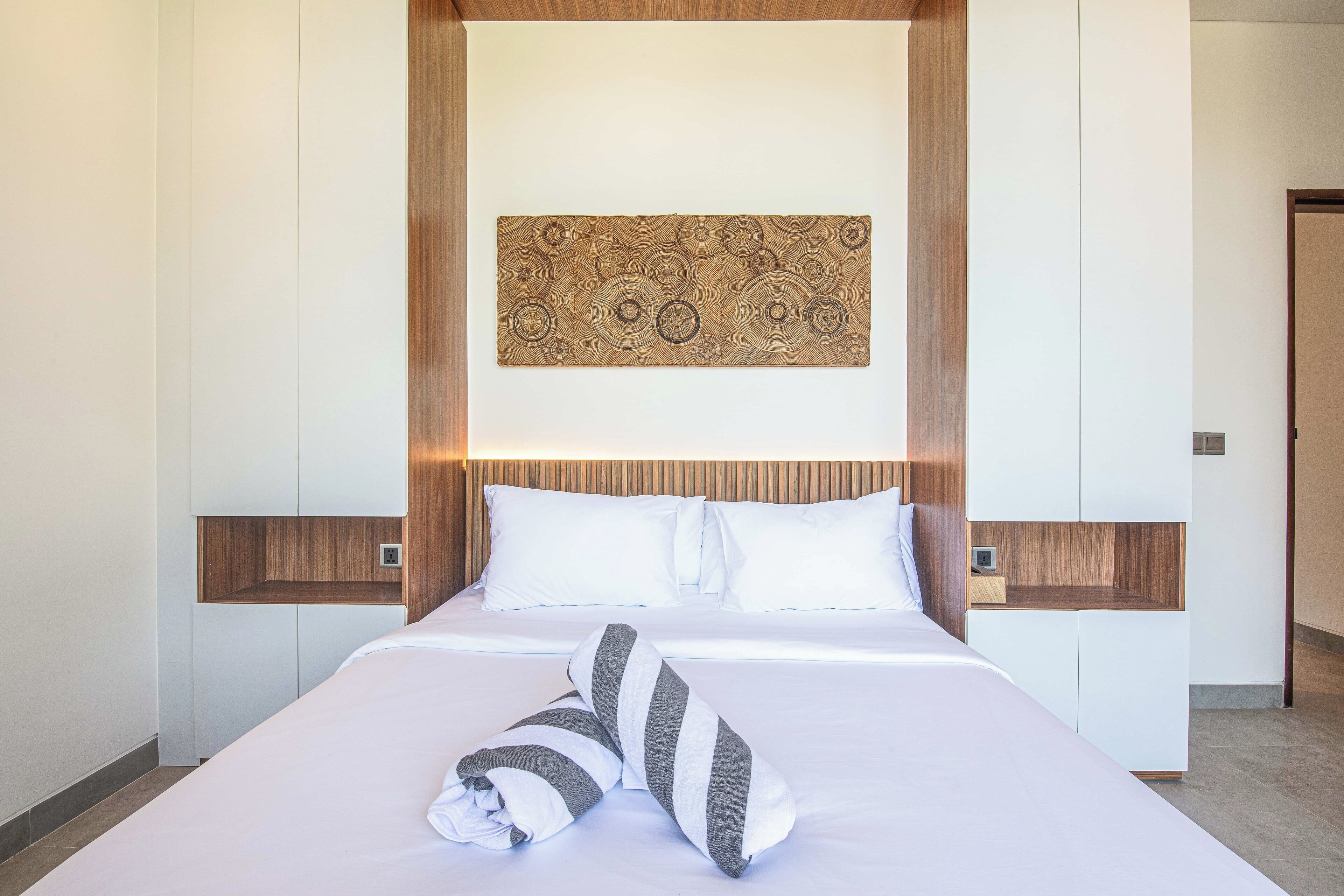 Une chambre d’hôtel moderne avec un lit bien fait, une tête de lit en bois et une œuvre d’art accrochée au mur.