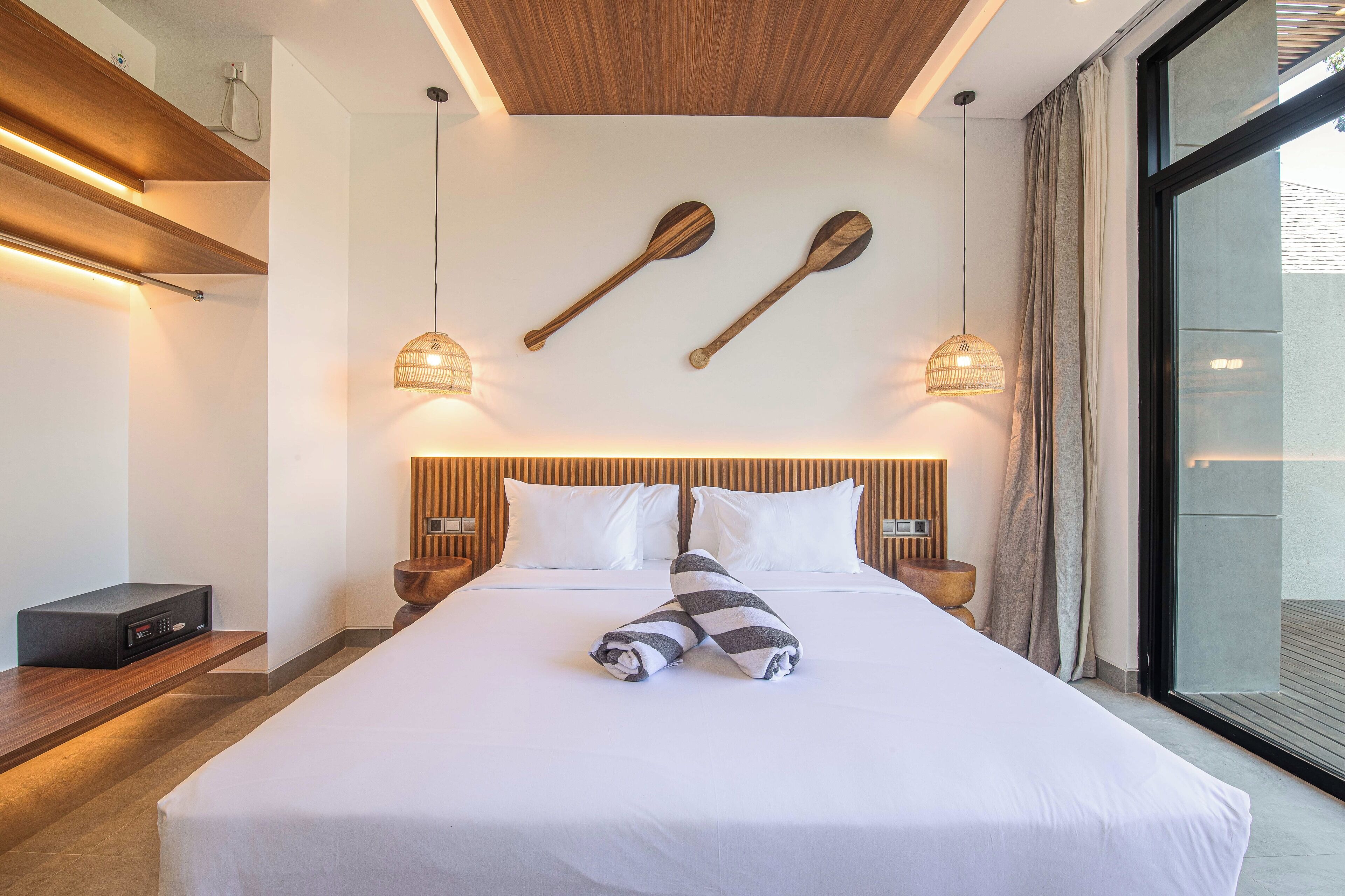 Una moderna camera d'albergo con un letto grande, una testiera in legno, due luci a parete e una vista attraverso una porta di vetro.