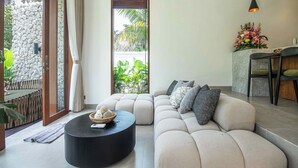 A modern living room with a beige sofa, a black round coffee table, and a stone wall. - Chic 1BR Villa Jungle Escape Heart of Ubud (Ubud)