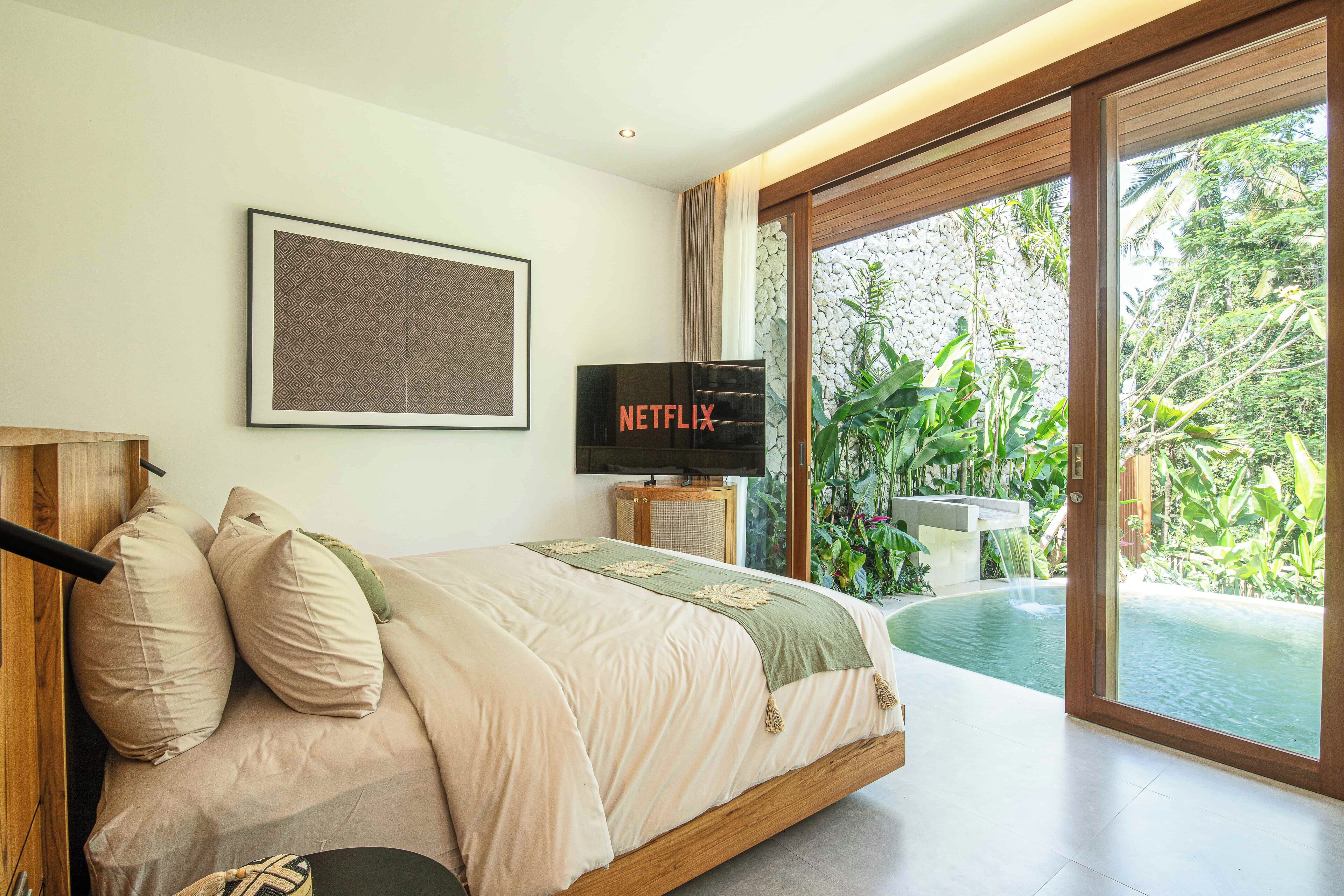 Een slaapkamer met een bed, een televisie en uitzicht op een zwembad en groen.