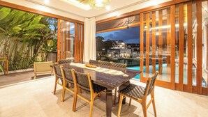 Un comedor con vista a la piscina, muebles de madera y un ventanal grande.