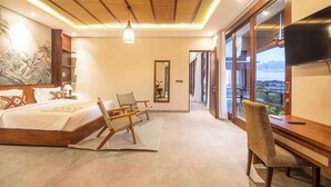 Un dormitorio con cama, dos sillas, escritorio, televisor y ventana grande con vistas.