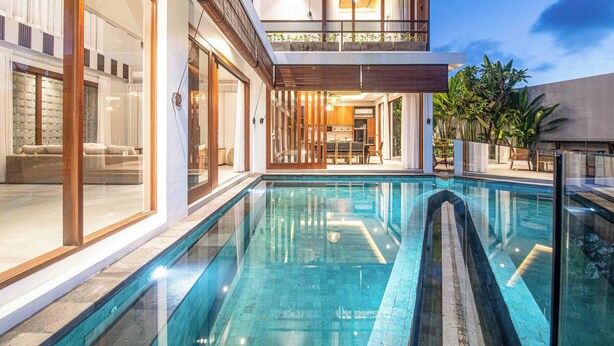 Una casa moderna de dos pisos con piscina, ventanas amplias y un balcón.