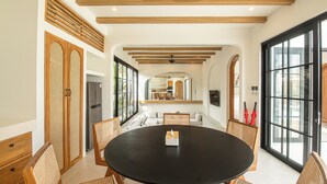 Un espace repas moderne avec une table ronde, des chaises en bois et une nappe noire. On aperçoit un réfrigérateur et un meuble en bois à l’arrière-plan.