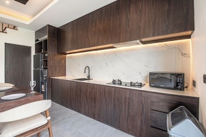 A modern kitchen with dark wood cabinetry, a marble countertop, a built-in microwave, and a stainless steel sink. - Elegant 5BR Tropical Escape Just 400 m to Beach (Canggu)