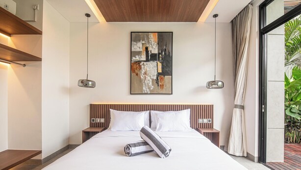 Een moderne hotelkamer met een groot bed, een houten hoofdbord en een groot abstract schilderij erboven.