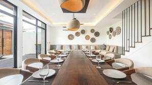 Een moderne eetruimte met een lange houten tafel, meerdere stoelen en een hanglamp.