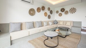 Een moderne woonkamer met een beige bank, gestreepte kussens, een glazen salontafel en decoratieve wanddecoratie.