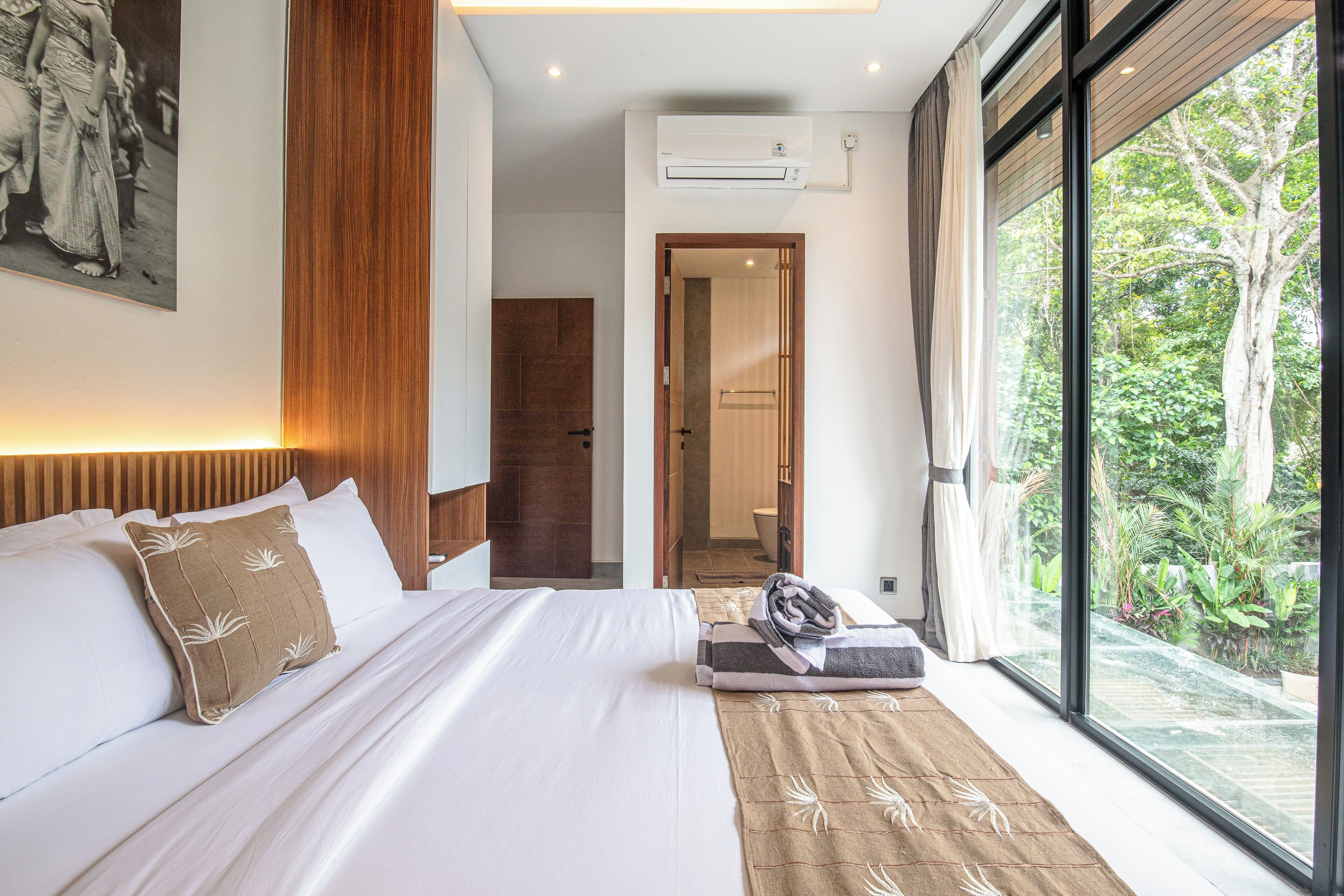 Una camera d'albergo moderna con un letto grande, vista su spazi verdi e una testiera in legno.