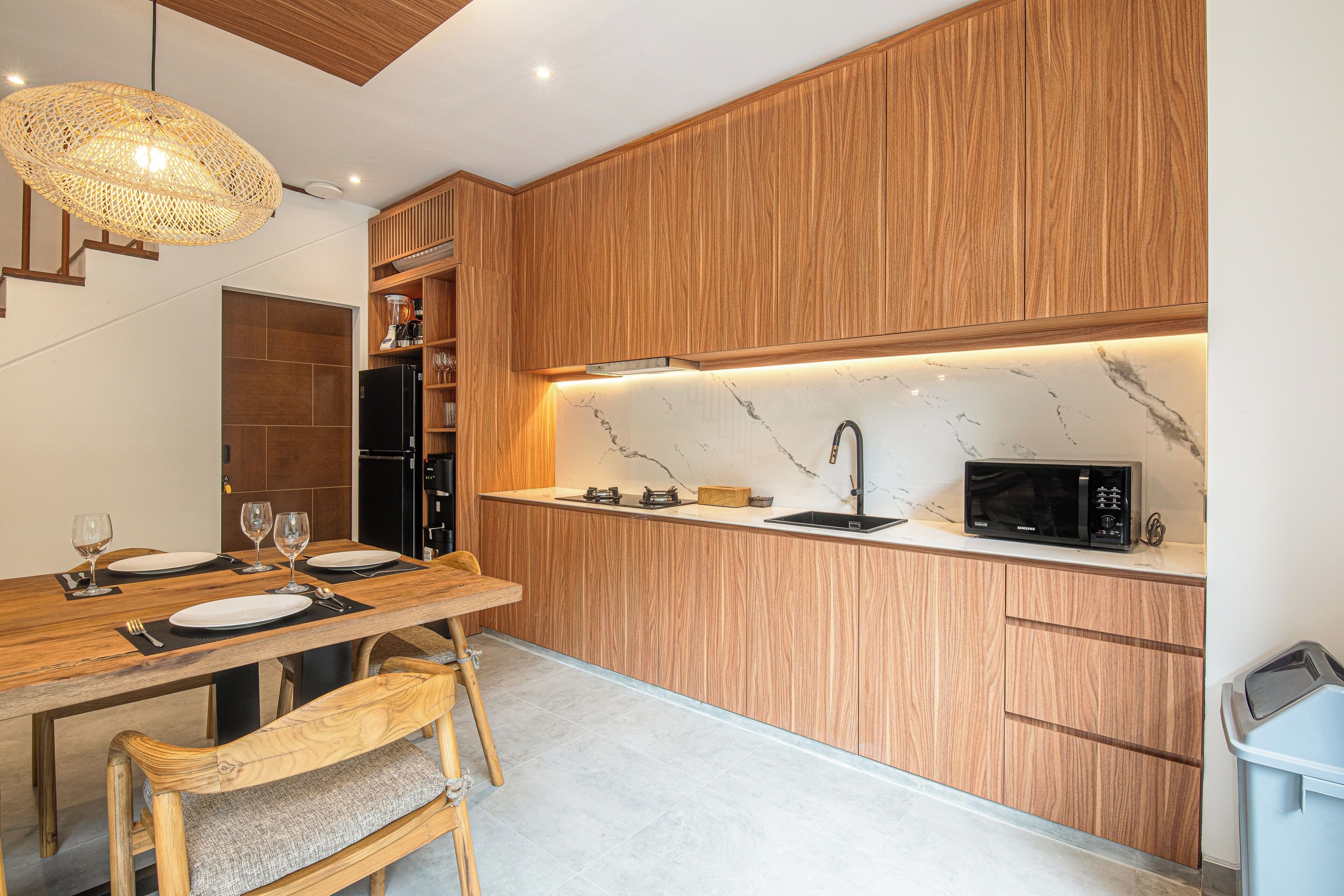 A modern kitchen with wooden cabinetry, a marble countertop, and a built-in microwave.