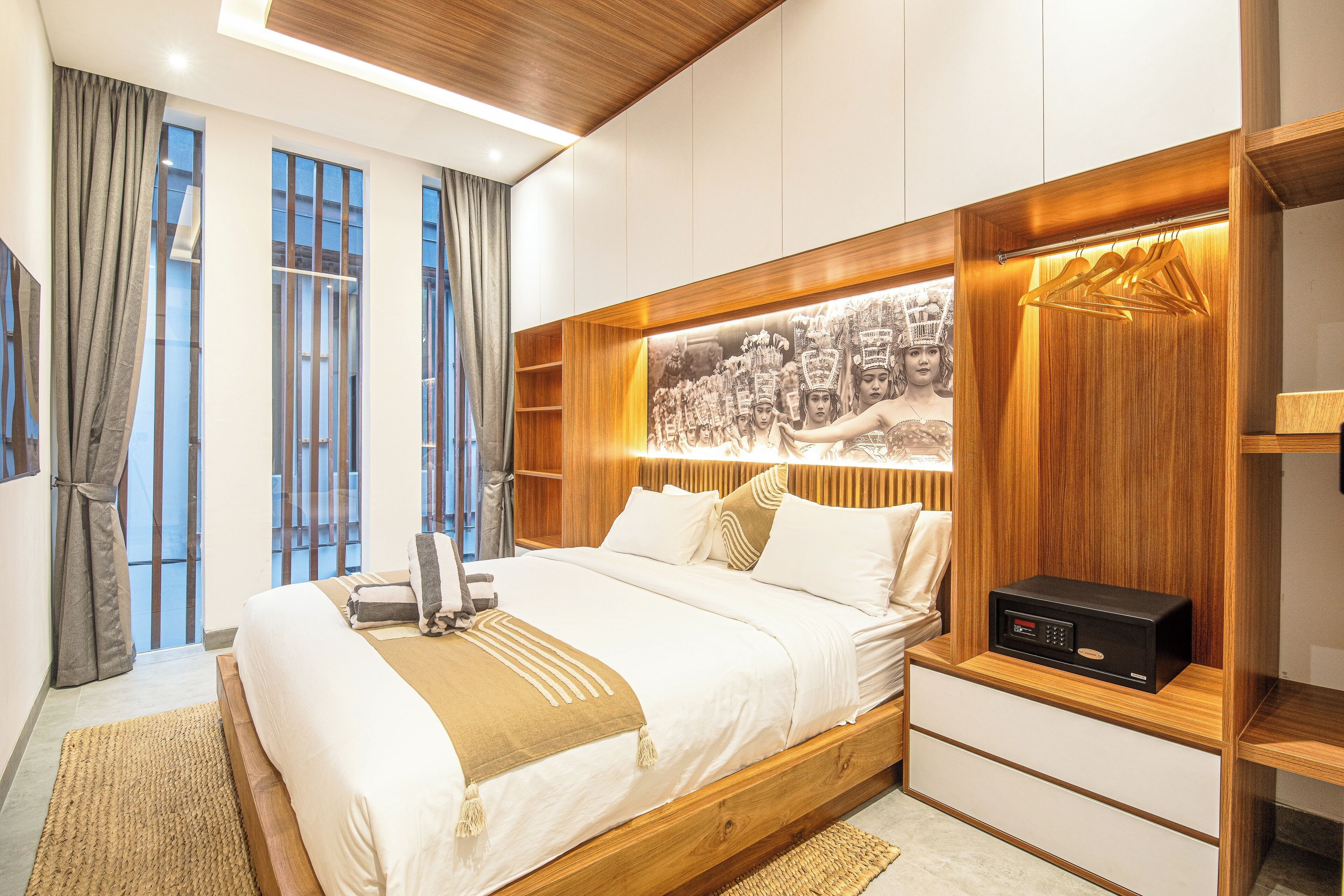 Une chambre moderne avec un grand lit, une tête de lit en bois, une horloge numérique et une vue sur le balcon.