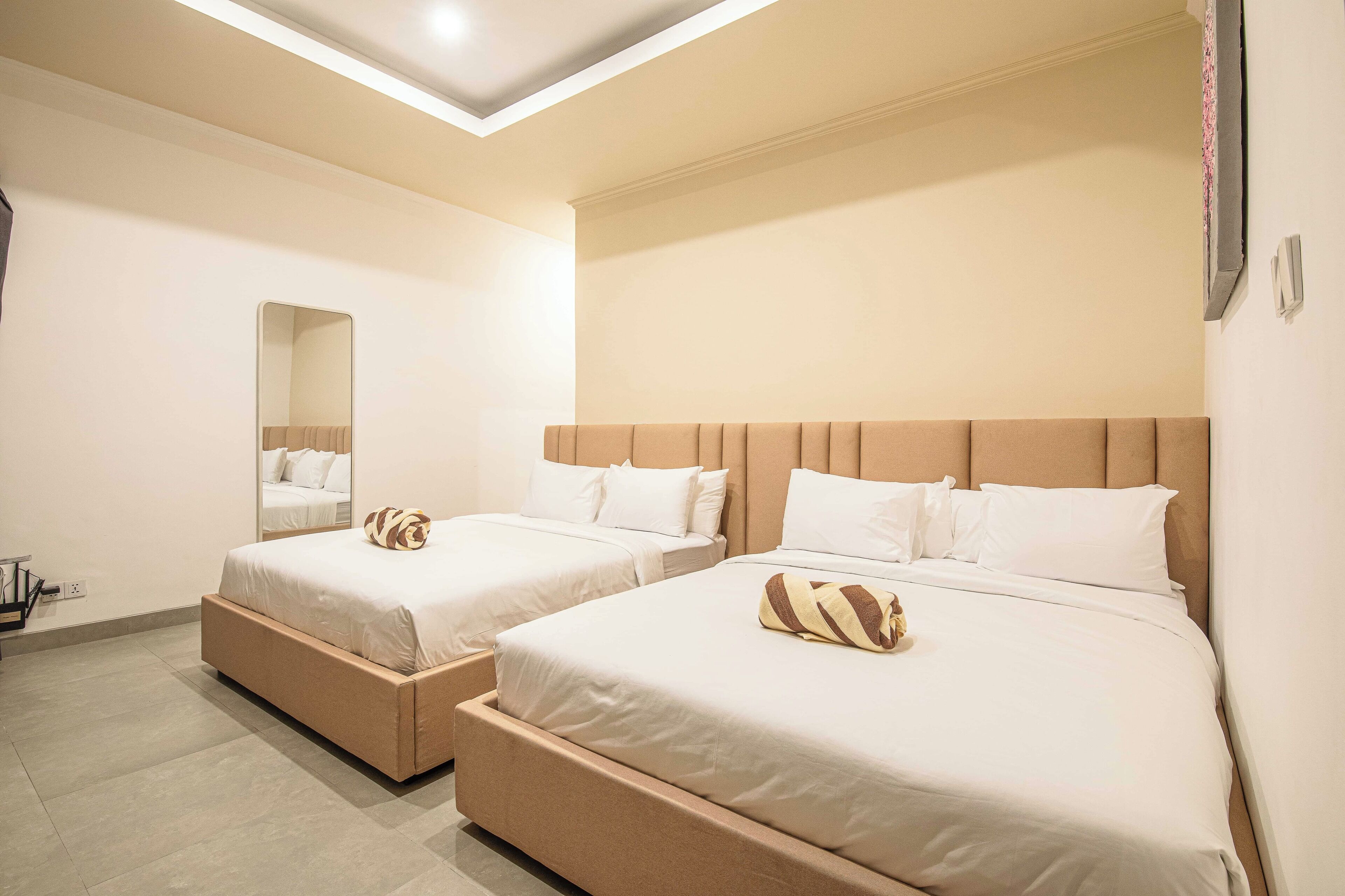 Een hotelkamer met twee bedden, een grote spiegel en een modern plafondontwerp.