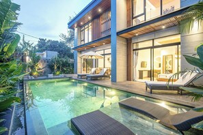 A modern house with a swimming pool, lounge chairs, and a well-lit outdoor area. - Elegant 5BR Modern Villa Steps From Caf Del Mar (Seminyak)