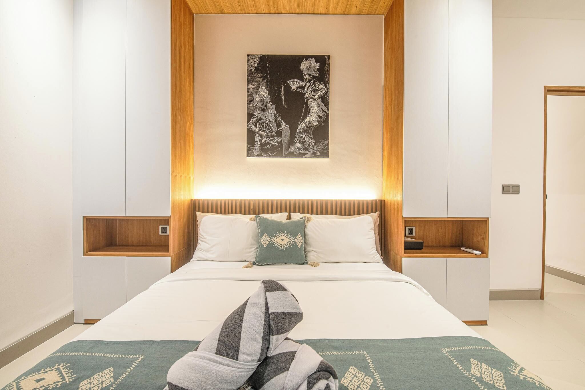 A modern hotel room with a large bed, wooden headboard, and a framed artwork above the bed.