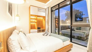 A modern bedroom with a large bed, a wooden headboard, a bedside table, and a large window with a view of the outside. - Elegant 5BR Modern Villa Steps From Caf Del Mar (Seminyak)