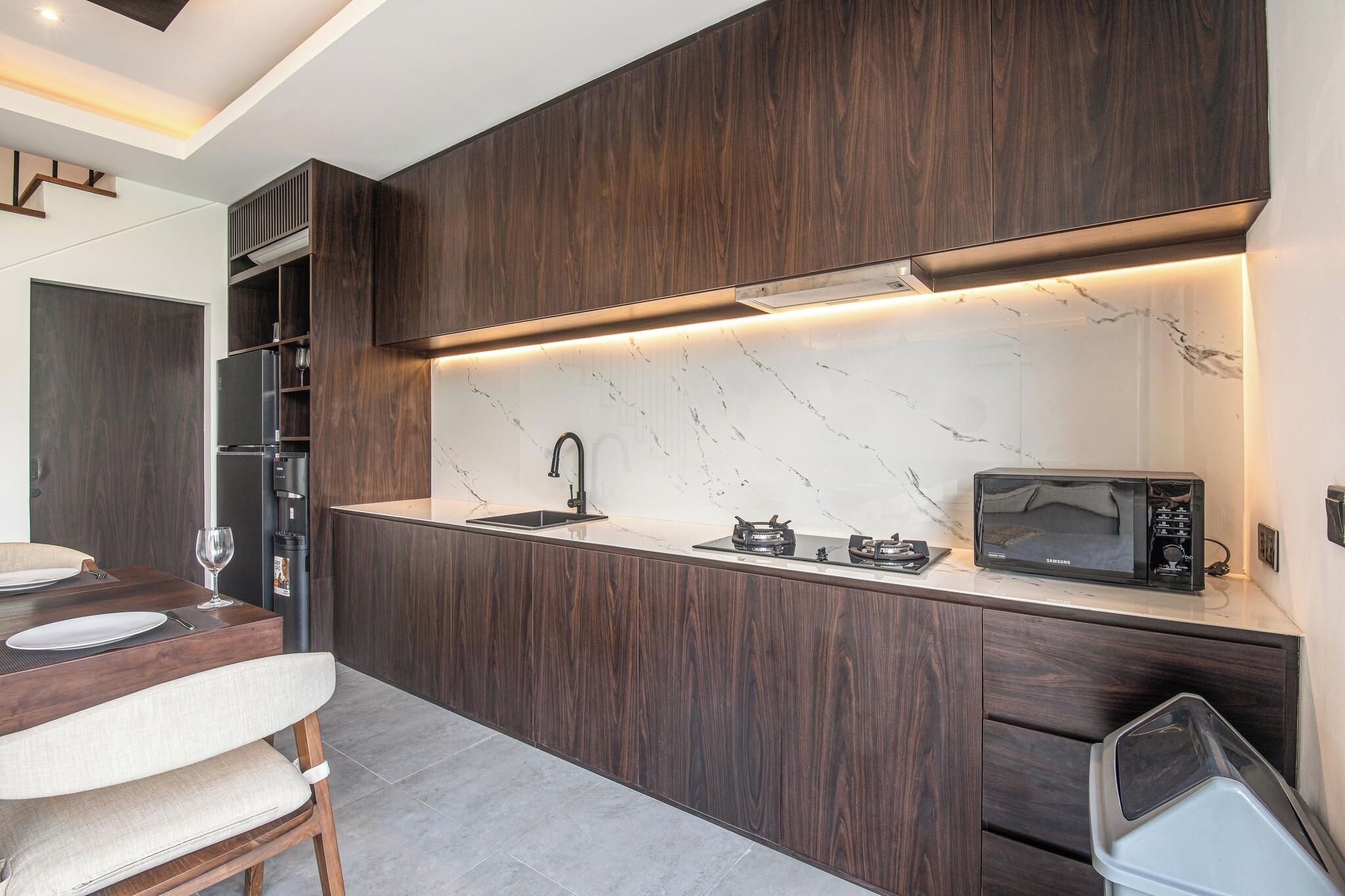 A modern kitchen with dark wood cabinetry, a marble countertop, and a built-in microwave.