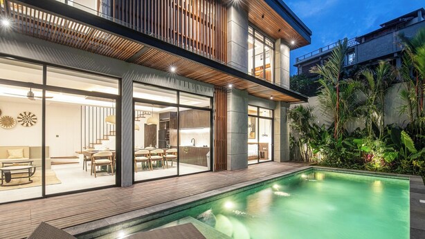 Una casa moderna con piscina, terraza de madera y puertas de cristal que dan a un comedor.