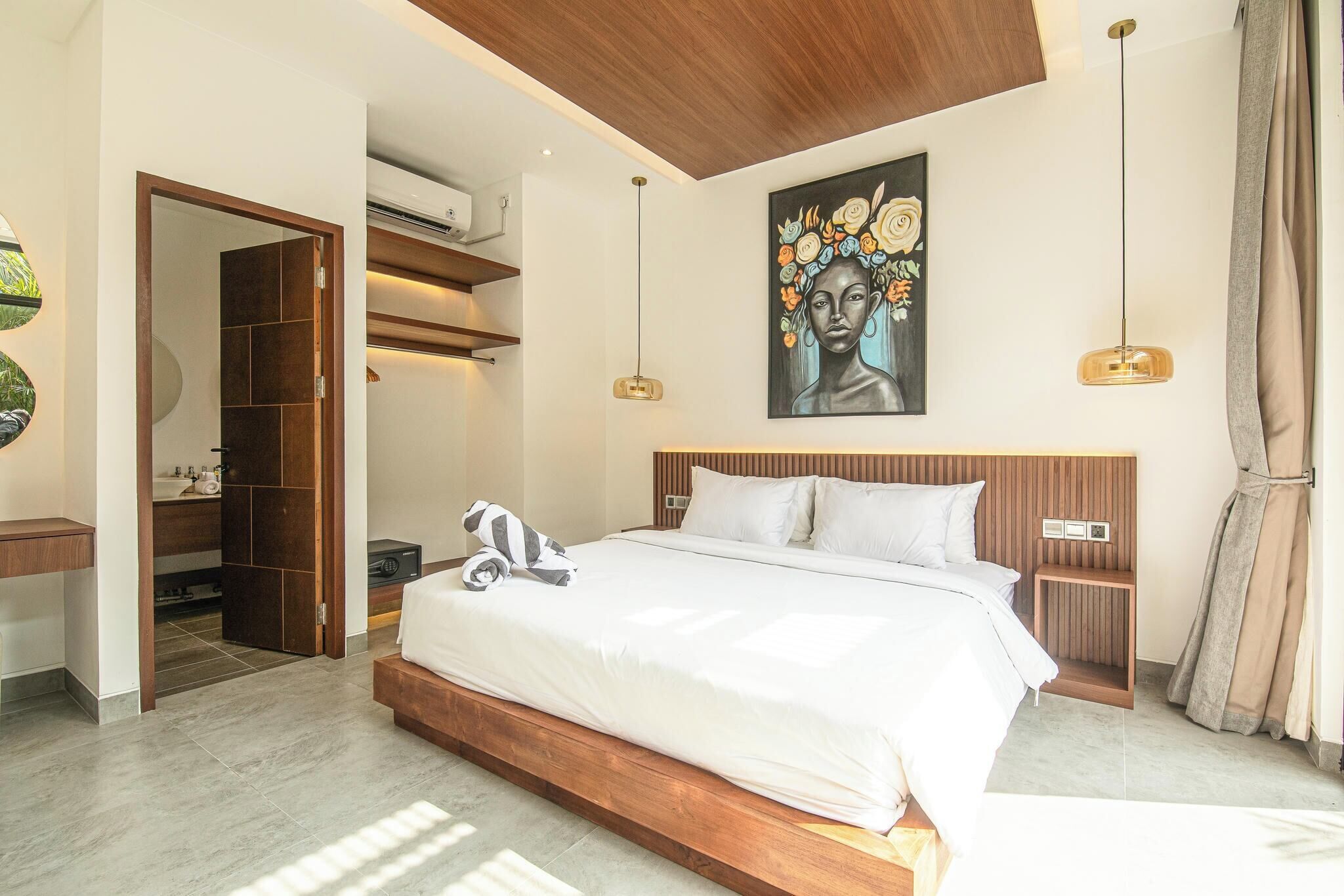 Ein modernes Hotelzimmer mit einem großen Bett, einem Holz-Kopfteil und einem Gemälde darüber. Ein Kleiderschrank mit Spiegel und ein kleiner Tisch neben dem Bett sind ebenfalls vorhanden.
