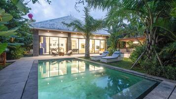 Een modern huis met een zwembad, terras en weelderige begroeiing.
