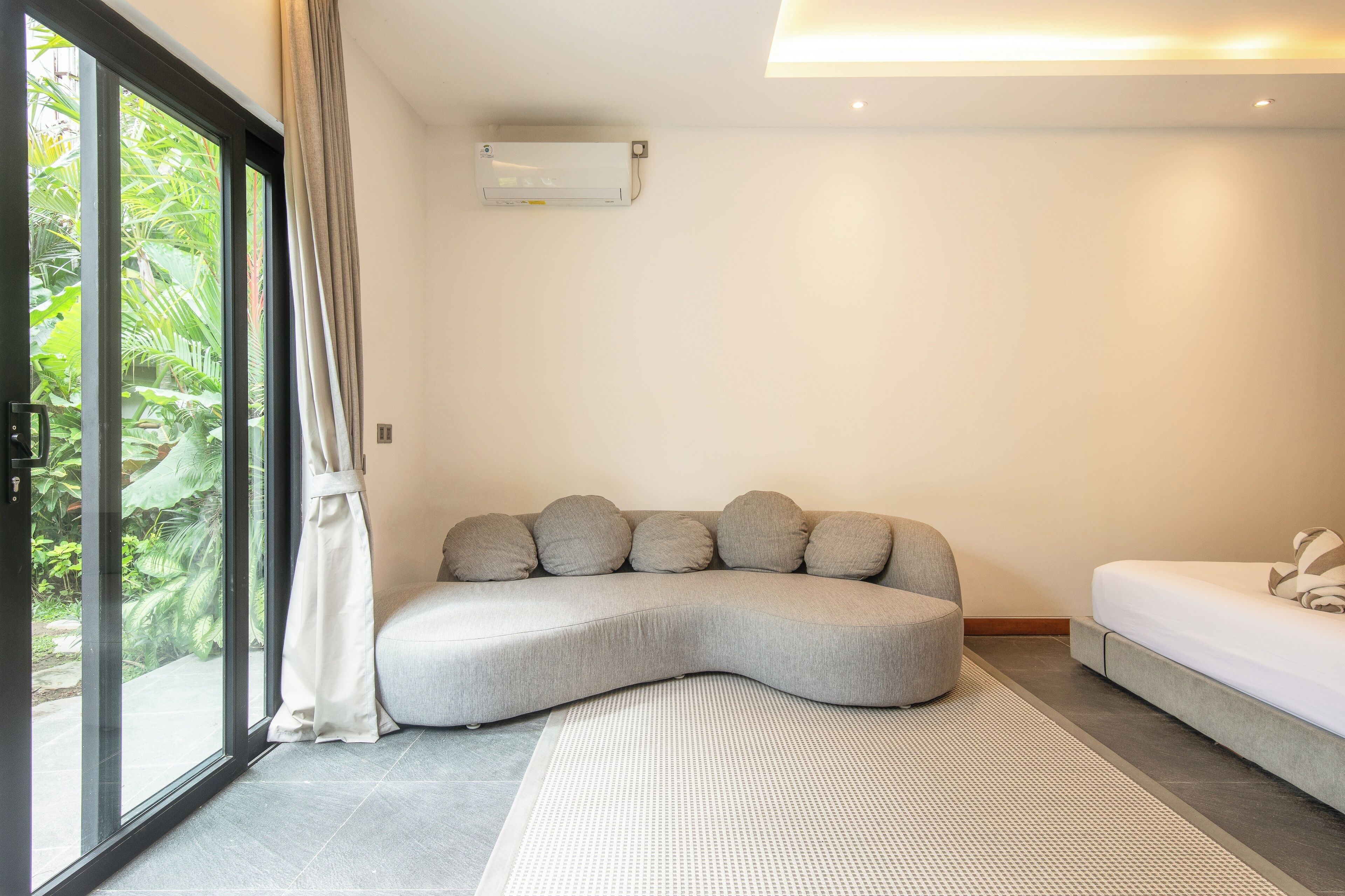 A modern living room with a curved sofa, a bed, and a large window with curtains.