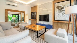 A modern living room with a wooden coffee table, grey sofas, a TV, and artwork on the walls. - Elegant 3BR Retreat Stylish Modern Villa Seminyak (Seminyak)