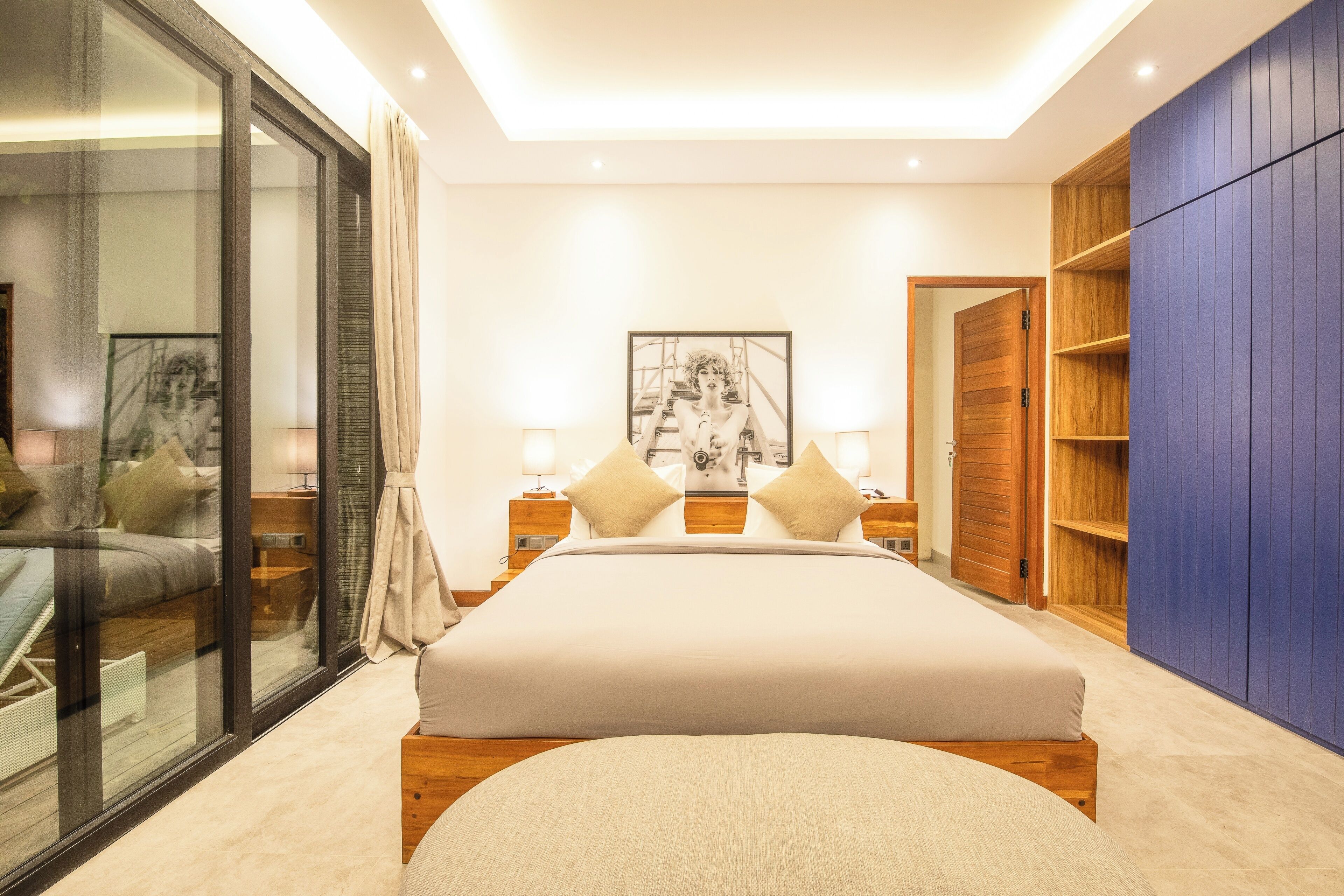 Quarto moderno com uma cama grande, mesas de cabeceira, guarda-roupa e porta de vidro para uma varanda.