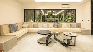 Ein modernes Wohnzimmer mit einem beigefarbenen Ecksofa, zwei Couchtischen mit Glasplatte und einem großen Fenster mit Blick auf Grünflächen.